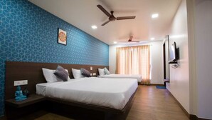Habitación de hotel con dos camas, ventilador de techo, televisión y pared con estampado.