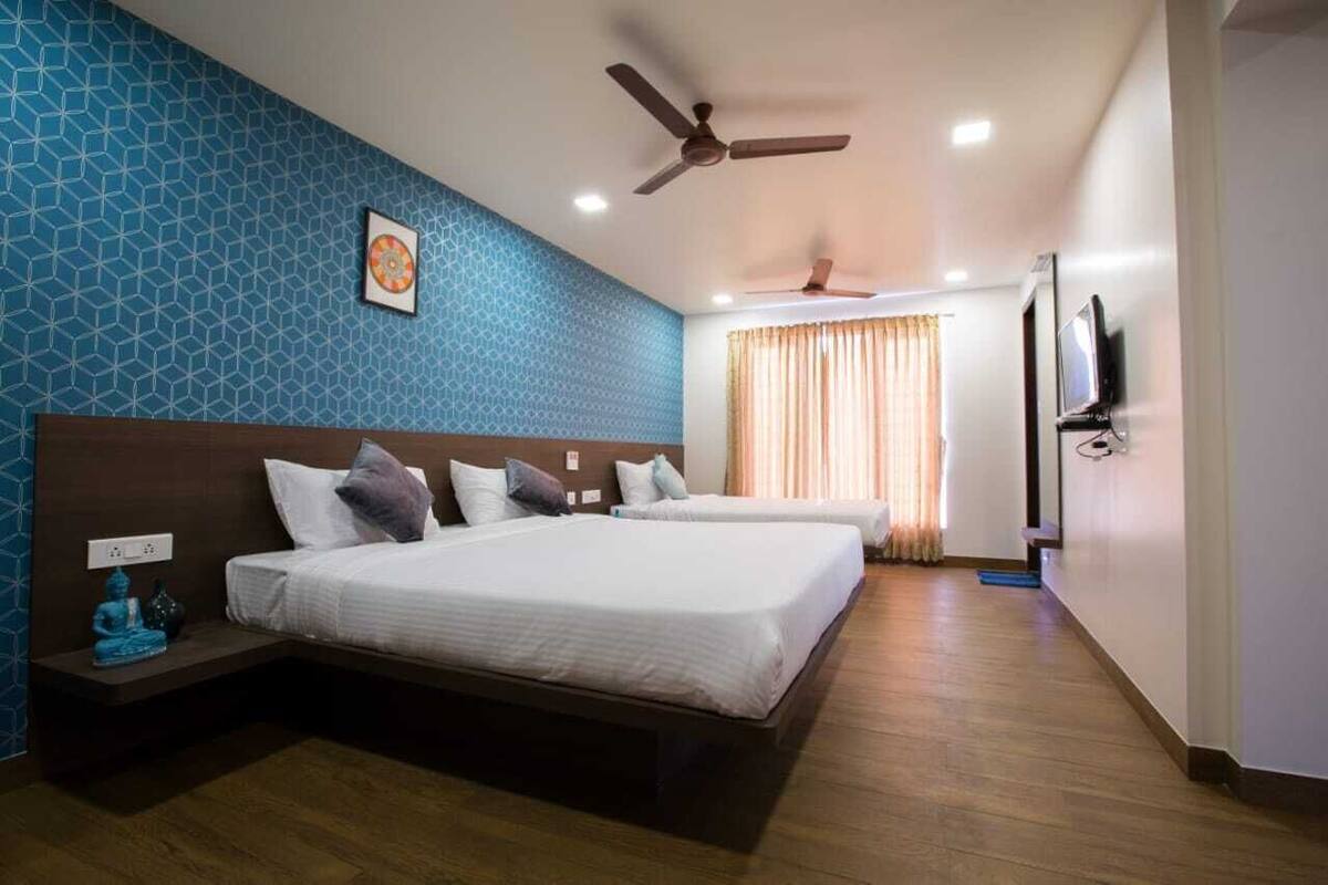A hotel room with two beds, a ceiling fan, a TV, and a patterned wall.
