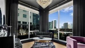A modern living room with a black sofa, a white coffee table, and a view of the cityscape through large windows.