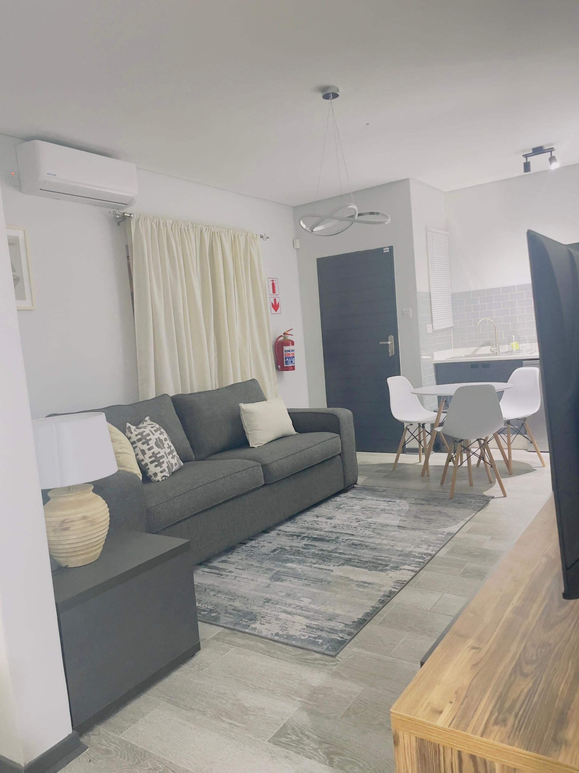 Un salon moderne avec un canapé gris, une table basse en bois et un coin repas avec des chaises blanches.
