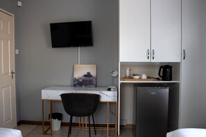 A hotel room with a desk, chair, bed, TV, and kitchenette.