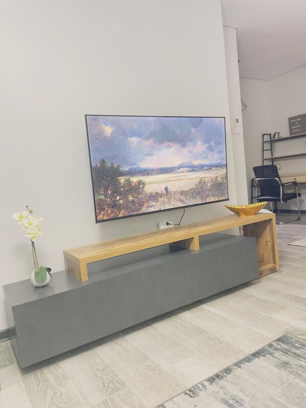 A modern living room with a flat-screen TV mounted on the wall, a wooden bench with a bowl, and a small potted plant.