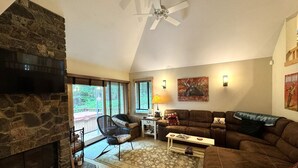 Ein Wohnzimmer mit Kamin aus Stein, einem braunen Ledersofa, einem Couchtisch und einem Deckenventilator.