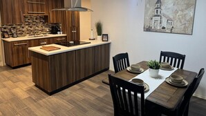 A modern kitchen with wooden cabinets, a central island, and a dining area with a table and chairs. - Mayberry Cozy Home (Mission)