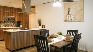 A modern kitchen with wooden cabinetry, a central island, and a dining area with four chairs and a table set for four. - Mayberry Cozy Home (Mission)
