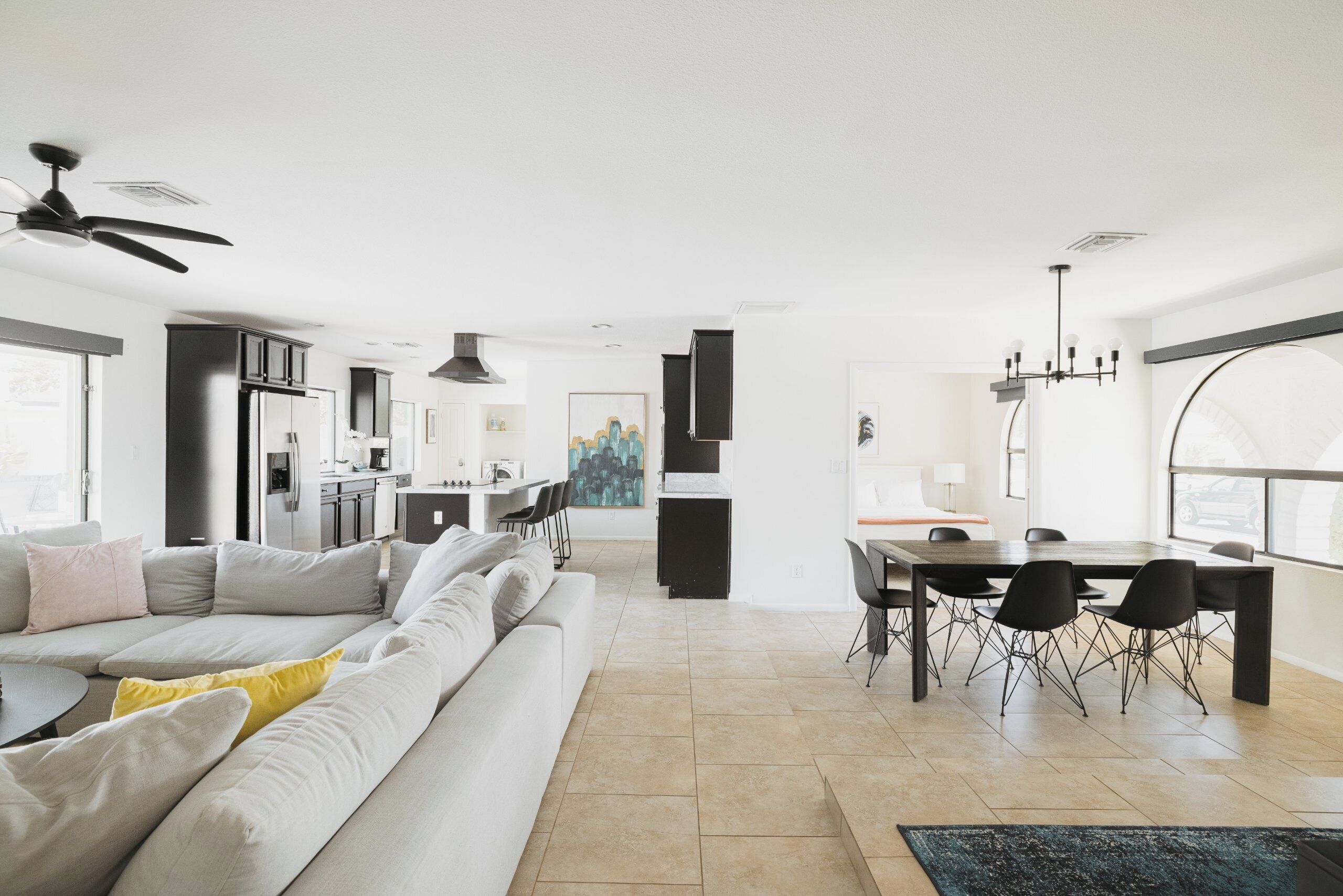 En moderne opholdsstue med sofa, spisebord og stole. Der er et køkkenområde med skabe og et køleskab.