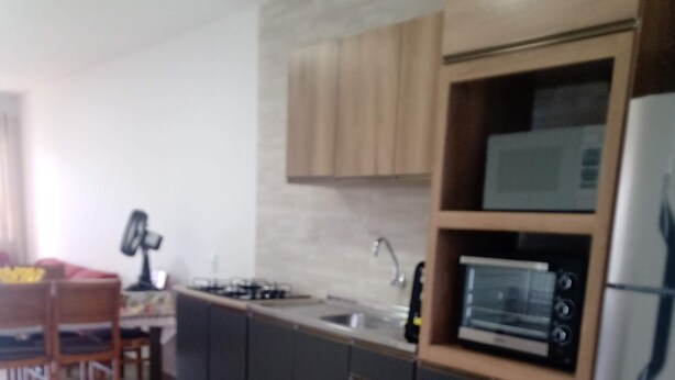 Una cocina moderna con microondas, horno y refrigerador integrados. Hay una mesa de comedor con sillas y un ventilador al fondo.