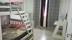 Una cama litera con escalera, un escritorio y una silla en una habitación con ventana y cortinas.