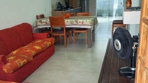 Un espacio habitable compacto con sofá, mesa de comedor, sillas, ventilador y zona de cocina.
