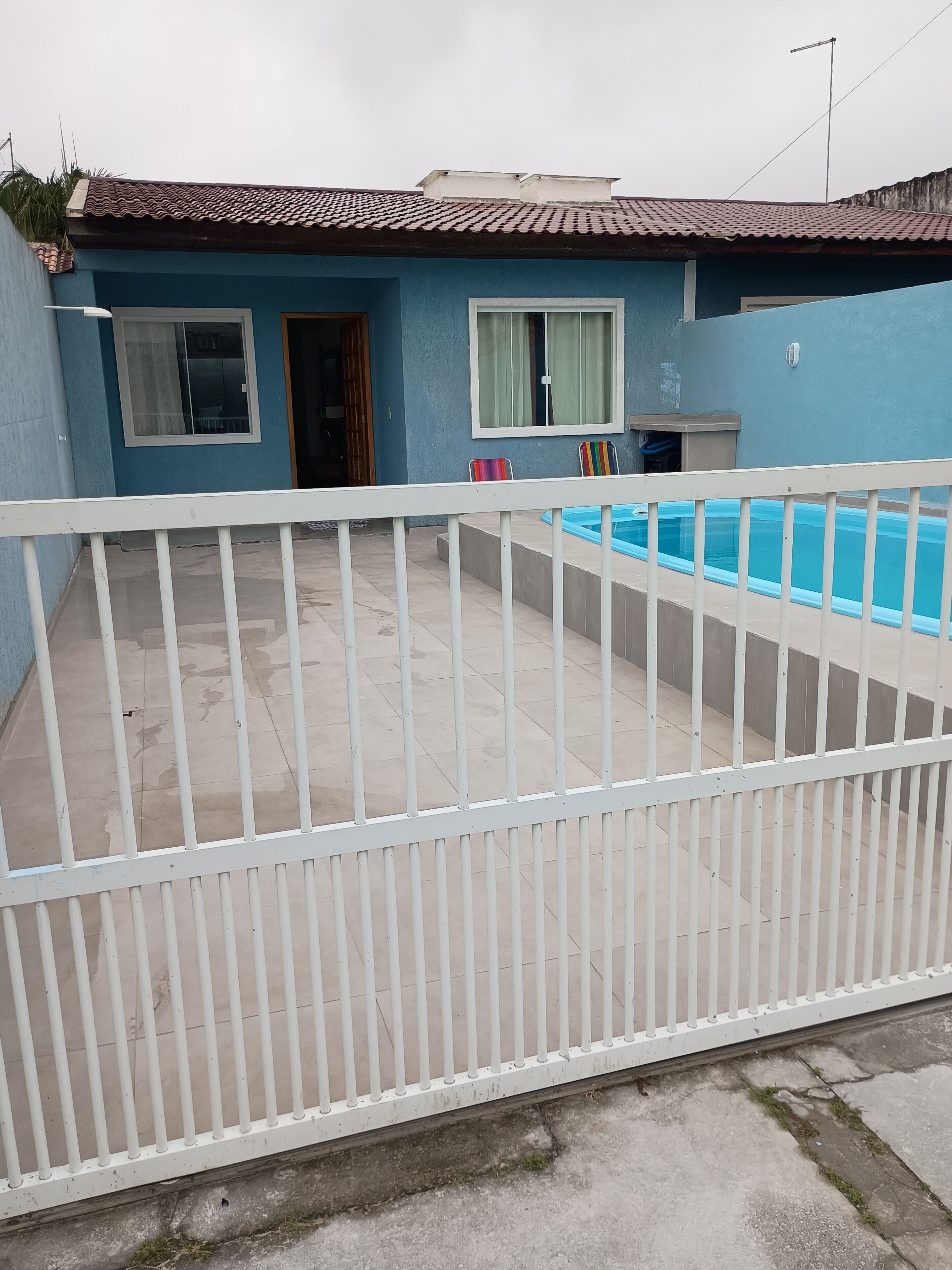 A residential property with a swimming pool, a blue exterior, and a white fence.