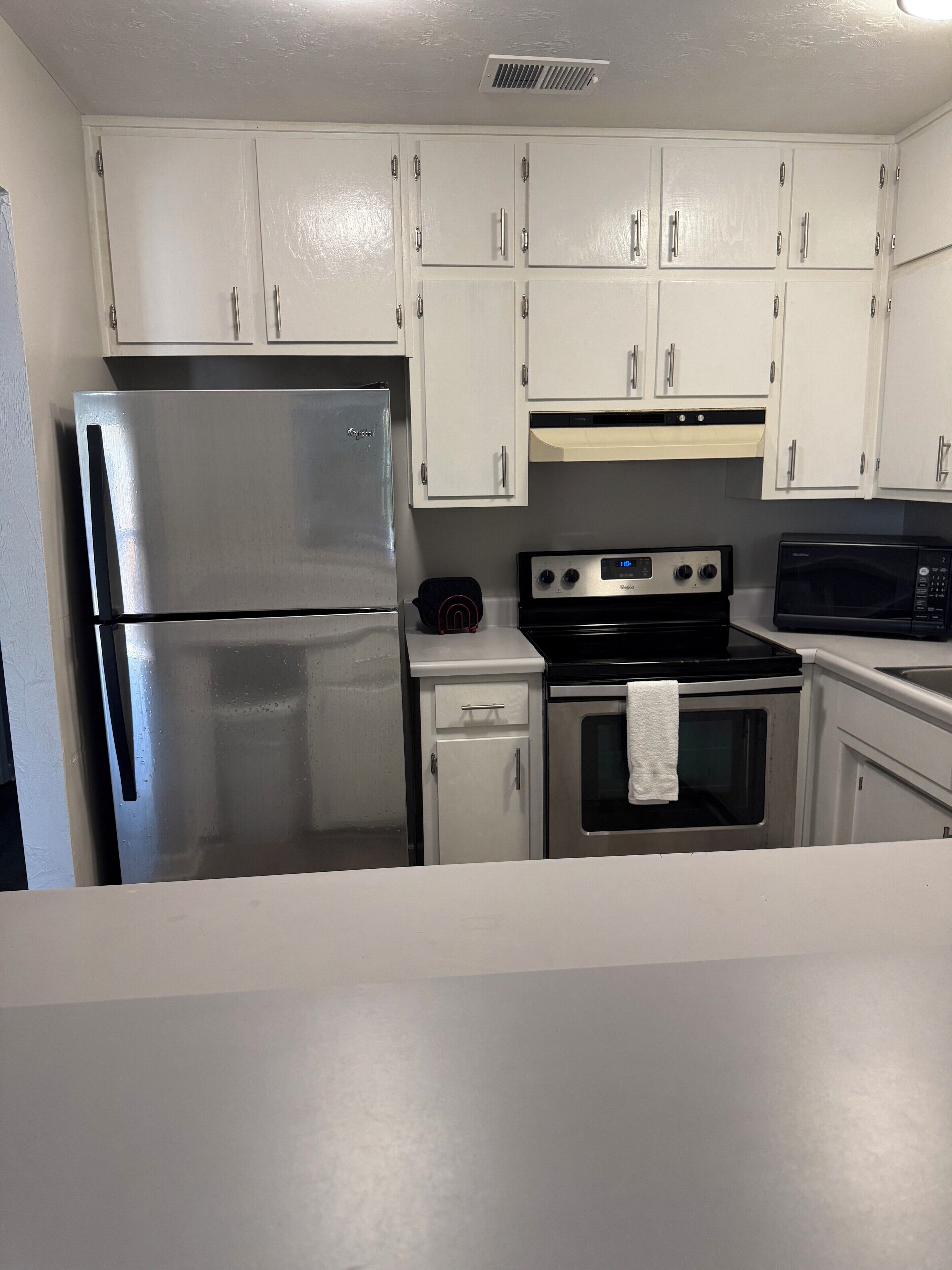 A compact kitchen with white cabinets, a stainless steel refrigerator, a microwave, and a stove.
