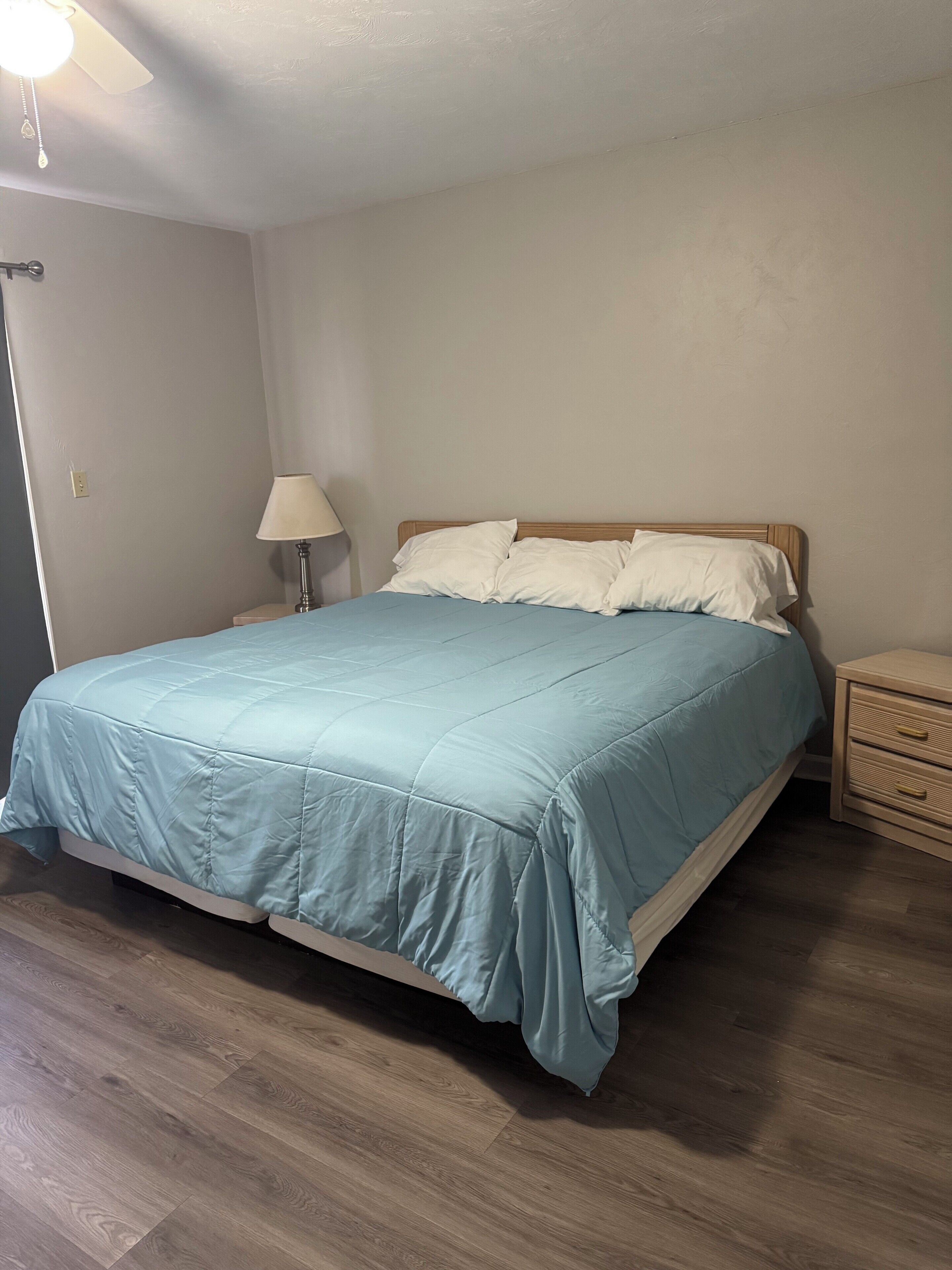 A bedroom with a bed, a nightstand, a lamp, and a ceiling fan.