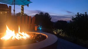 A fire pit with flames, a wooden bench, and a blue umbrella.