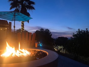 A fire pit with flames, a wooden bench, and a blue umbrella.