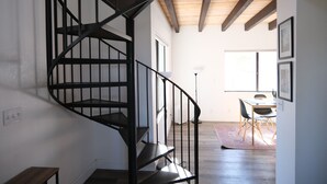 A spiral staircase with black railings leading to a dining area with a table and chairs.