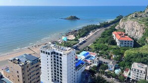 A coastal cityscape with a prominent white hotel, a beach, and a rocky outcrop in the distance. - HOTEL SON THINH VUNG TAU (Ho Chi Minh City)