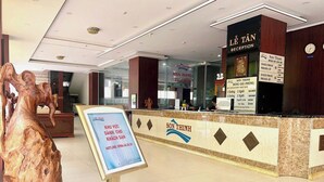 A reception area with a reception desk, a large wooden sculpture, and a signboard with hotel information. - HOTEL SON THINH VUNG TAU (Ho Chi Minh City)
