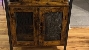 Puinen pöytä, jossa on verkkomainen etupaneeli, pullo giniä, Jenga-peli ja dominolaatikko.