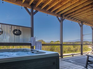Un bain à remous installé sous une pergola en bois, avec vue sur un vignoble et des montagnes.
