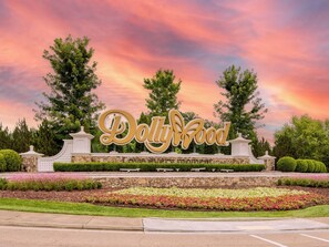 A sign with 'Dollywood' written in large letters, surrounded by landscaped gardens and trees.