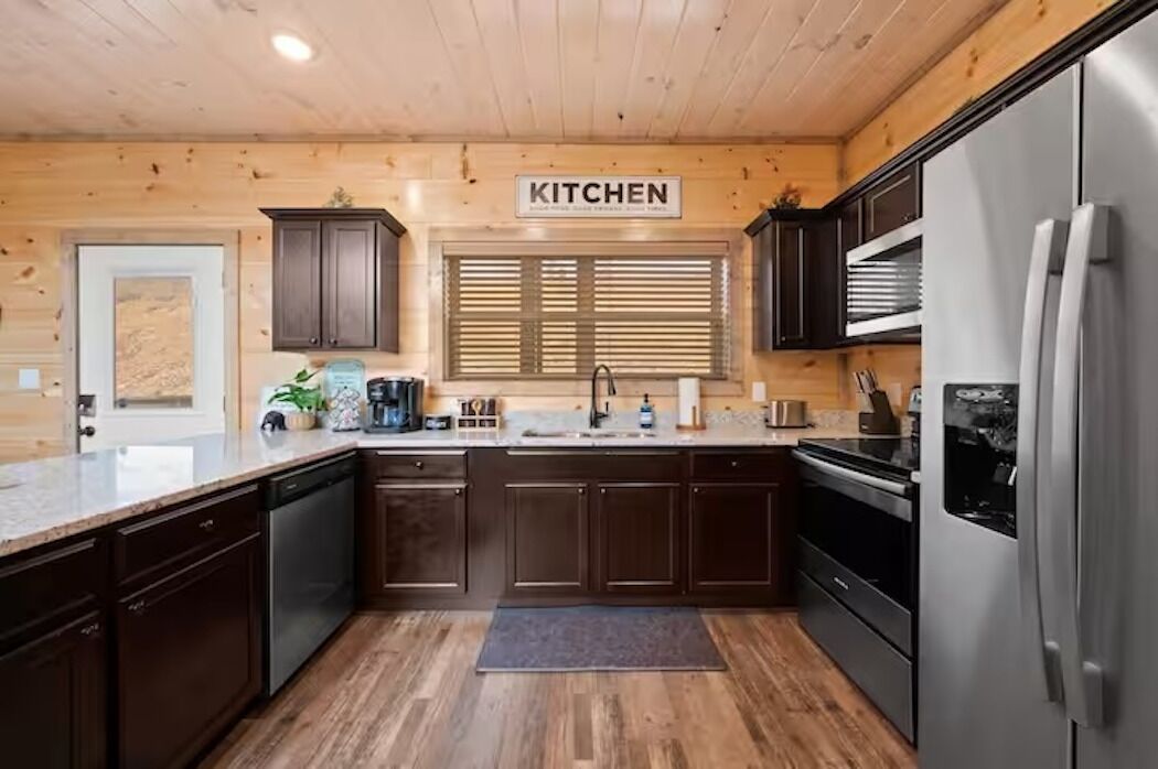 A modern kitchen with wooden cabinetry, a stainless steel refrigerator, and a window with blinds.