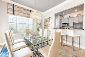 Un espace repas moderne avec une table en verre, des chaises blanches et un lustre.