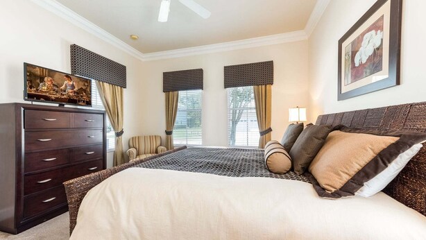 Hotelkamer met een bed, een dressoir, een stoel, een plafondventilator en een schilderij aan de muur.