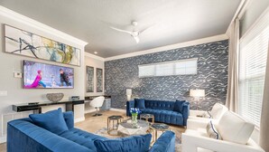Een moderne woonkamer met een blauwe bank, een witte fauteuil, een salontafel en een aan de muur bevestigde televisie.