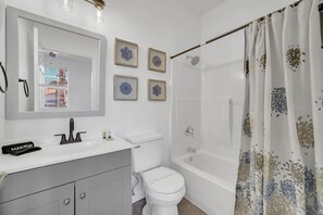 A bathroom with a white sink, mirror, and toilet. There are framed pictures on the wall, a shower curtain, and a towel rack. - Charming 3-bedroom townhome near to attractions (Clermont)