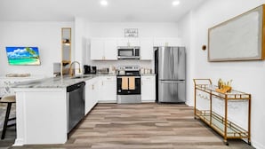 A modern kitchen with white cabinetry, stainless steel appliances, a marble countertop, and a gold cart with glasses. - Charming 3-bedroom townhome near to attractions (Clermont)