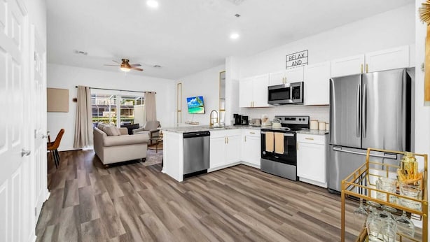 A modern kitchen with white cabinets, stainless steel appliances, and a dining area with a glass table. - Charming 3-bedroom townhome near to attractions (Clermont)