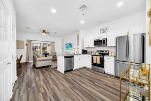 A modern kitchen with white cabinets, stainless steel appliances, and a dining area with a glass table. - Charming 3-bedroom townhome near to attractions (Clermont)