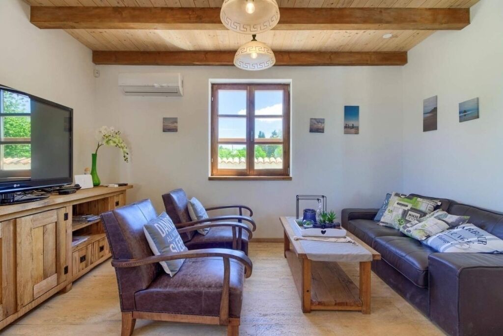 Una sala de estar con techo de madera, televisor, sofás de cuero, una mesa de centro y una ventana con vistas.