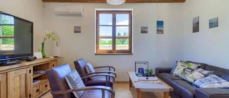 Una sala de estar con techo de madera, televisor, sofás de cuero, una mesa de centro y una ventana con vistas.
