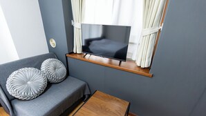 Un salon moderne avec un canapé gris, des coussins décoratifs, une petite table en bois et un téléviseur fixé au mur.