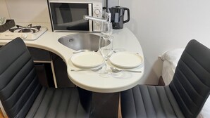 Une petite cuisine équipée d’un four à micro-ondes, d’une bouilloire et d’une cuisinière à gaz. On y trouve également un petit évier et une table ronde avec deux chaises.