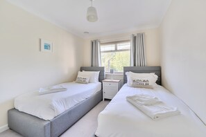 A bedroom with two single beds, a bedside table with a lamp, and a window with curtains. - Sleeps 9- KingBeds- FamilyFriendly- ContactlessCI (Wadebridge)