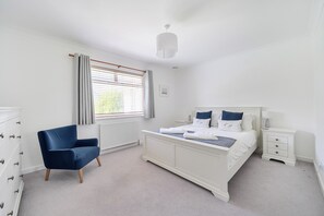 A bedroom with a bed, a chair, a nightstand, and a window with blinds.