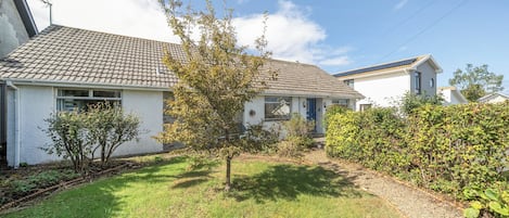 A residential property with a tiled roof, a small garden with a tree, and a hedge.