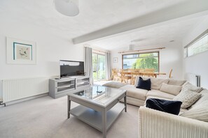 A modern living room with a flat-screen TV, a glass coffee table, a sofa, and a dining area with wooden chairs. - Sleeps 9- KingBeds- FamilyFriendly- ContactlessCI (Wadebridge)