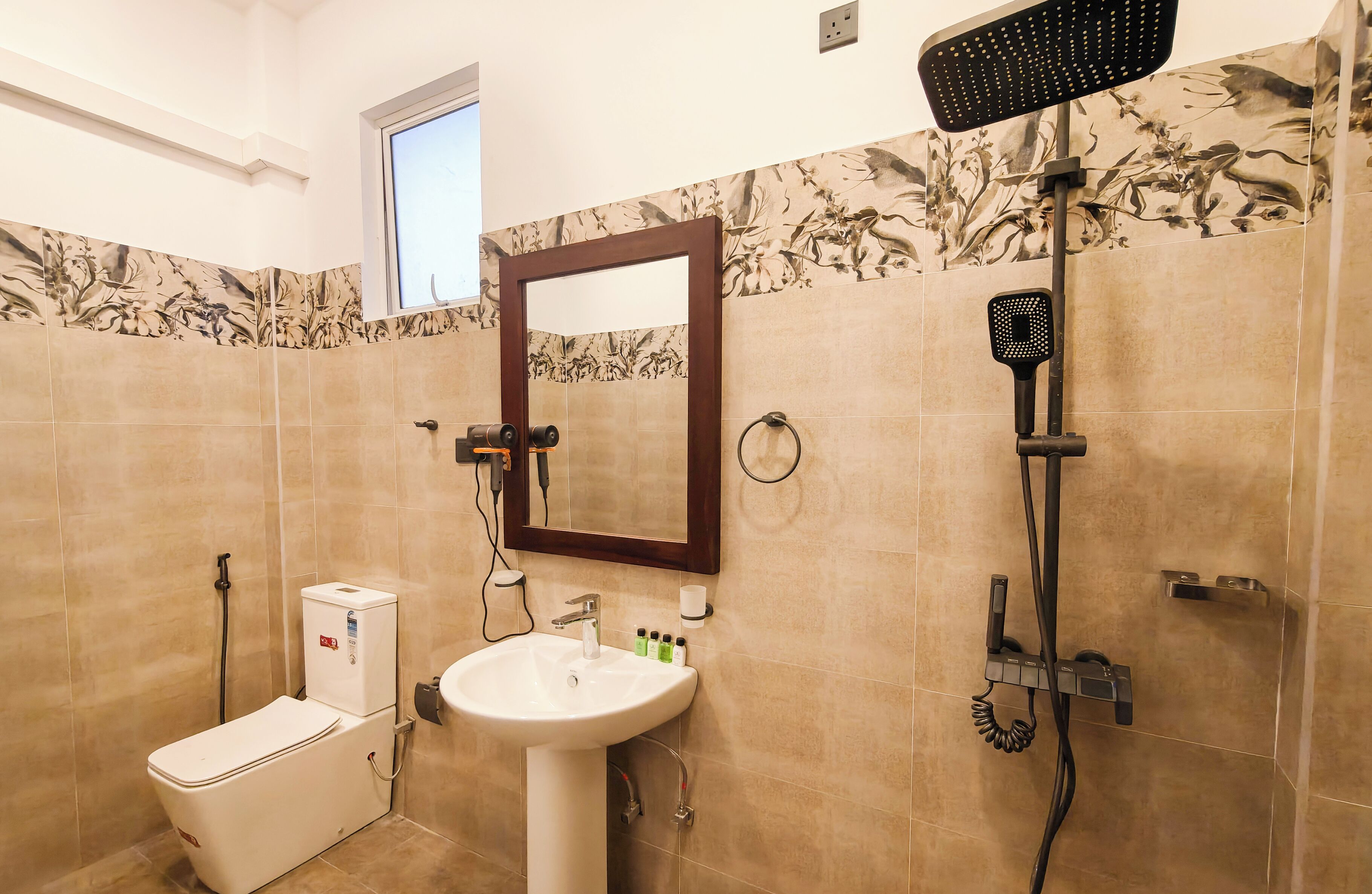 A bathroom with a toilet, sink, mirror, shower, and decorative tiles.