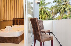 A bedroom with a bed, a chair, and a view of palm trees. - Sasnidu Villa (Hikkaduwa)