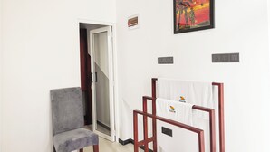 Une pièce avec un fauteuil gris, une chaise en bois sur laquelle est posée une serviette, un tableau et une porte qui donne sur une autre pièce.