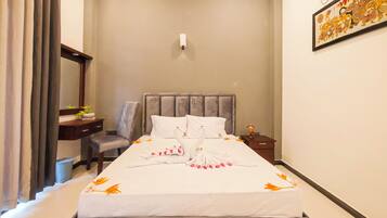 A hotel room with a bed, a desk, a chair, a nightstand, and a wall-mounted light.