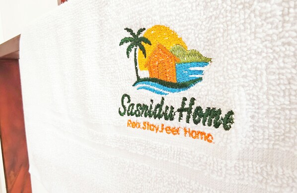 A towel with an embroidered logo and text reading "Sandiut House" and "Enjoy Stay Here Home." - Sasnidu Villa (Hikkaduwa)