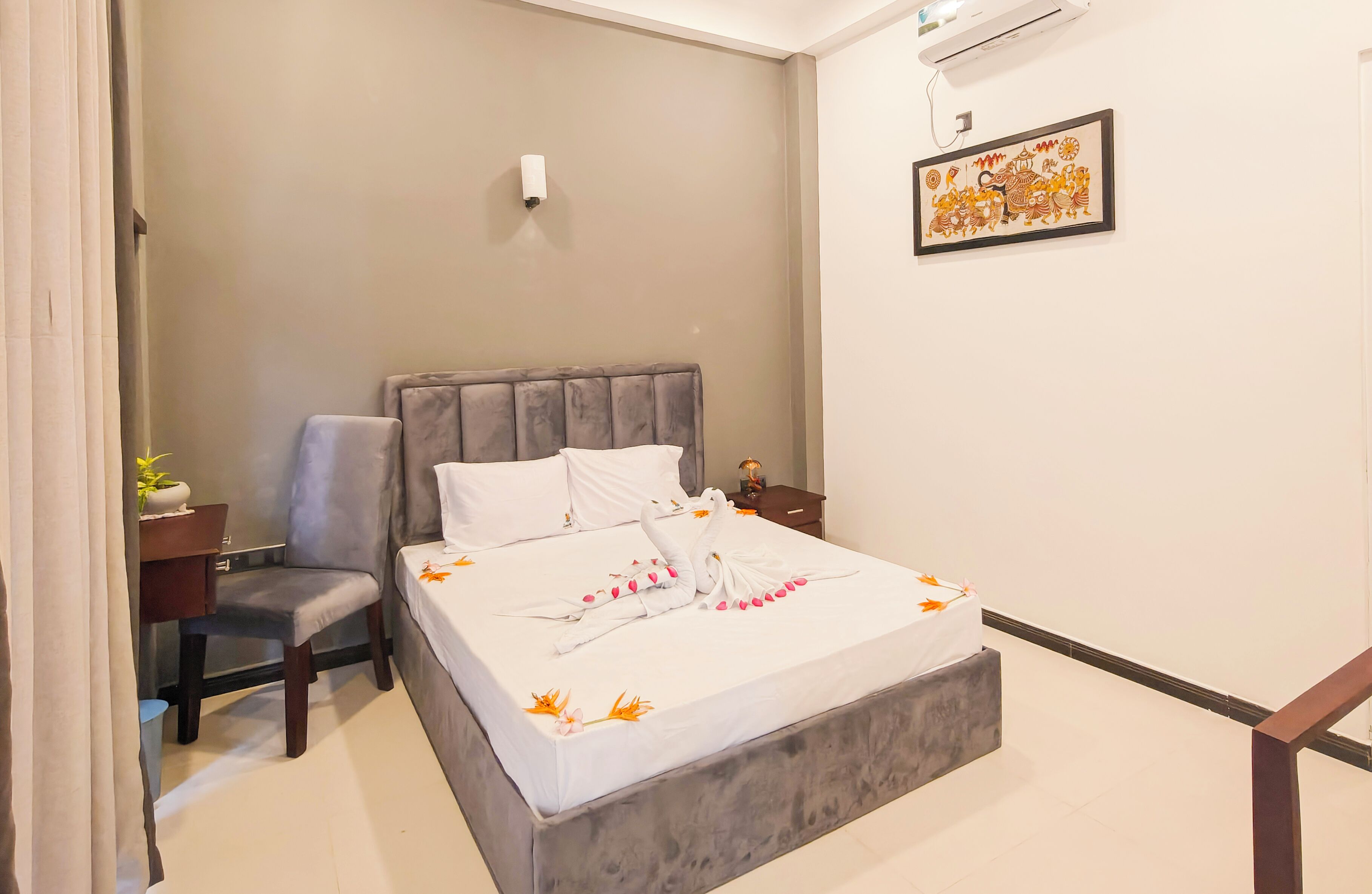 A neatly made bed with a grey headboard, a bedside table with a lamp, and a wall-mounted artwork.