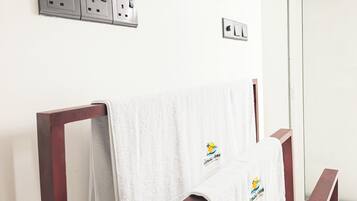 Un baño con una toalla blanca colgada en una silla de madera, un perchero y un enchufe en la pared.