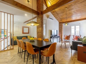 A spacious dining area with a wooden table, orange chairs, and a brick wall.