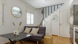 Una sala de estar moderna con un sofá, una mesa de vidrio, un tapete pequeño y una escalera que sube a otro nivel.