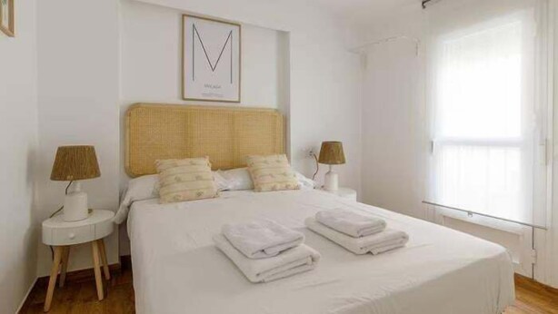 Un dormitorio ordenado con una cama grande, dos mesitas de noche y una ventana con cortinas.